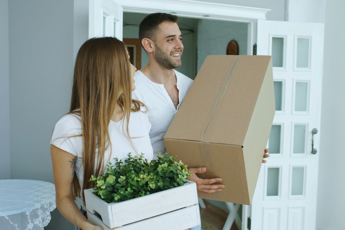 Paar trägt Umzugskartons und eine Pflanze in die neue Wohnung